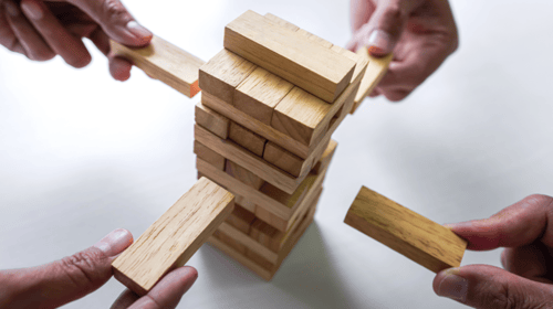 Different hands photographed playing a game of Jenga. Blogpost about Corporate Entrepreneurship strategy.